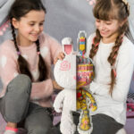 two girls sitting on a blanket holding a toy