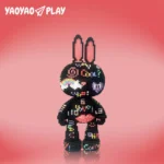 A glossy black ​​Brick Bear toy​​ with rainbow arcs and heart motifs on a gradient pink backdrop.